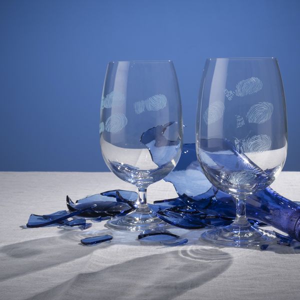 Two wine glasses with engraved fingerprints and a shattered blue glass bottle