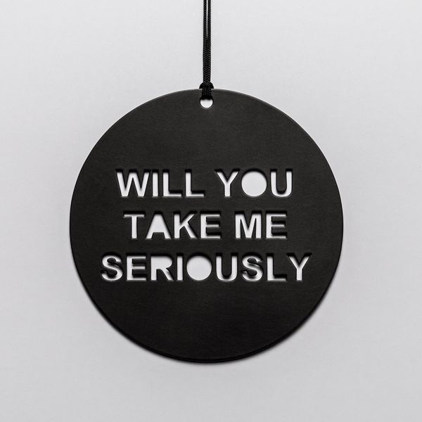 Black circular metal disk with the words "Will you take me seriously" cut out